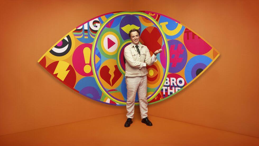Big Brother 2023 housemate Henry standing in front of the new eye logo with a bright orange background.