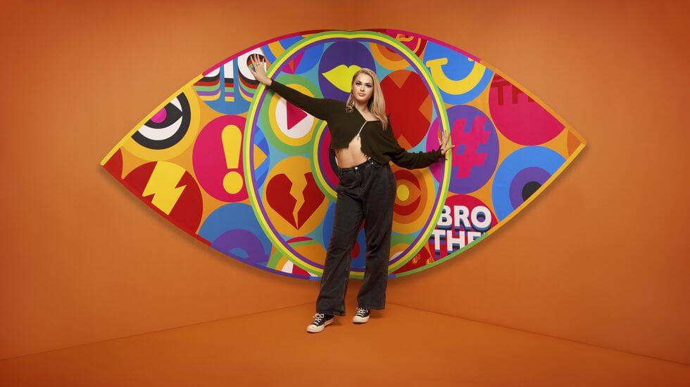 Big Brother 2023 housemate Hallie standing in front of the new eye logo with a bright orange background.