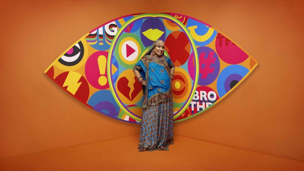 Big Brother 2023 housemate Farida standing in front of the new eye logo with a bright orange background.