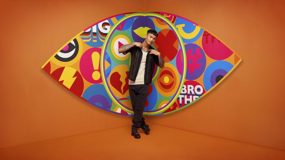 Big Brother 2023 housemate Zak standing in front of the new eye logo with a bright orange background.