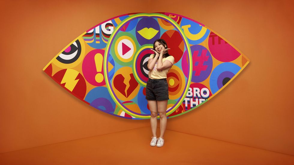 Big Brother 2023 housemate Yinrun standing in front of the new eye logo with a bright orange background.