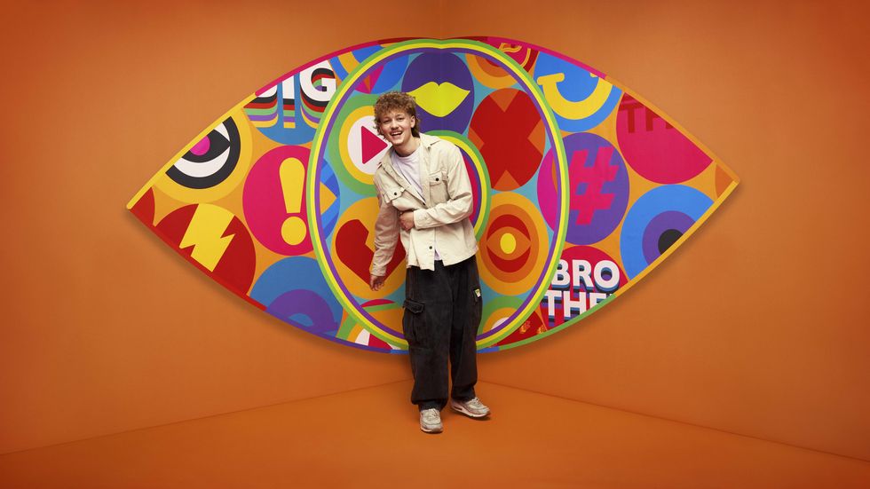 Big Brother 2023 housemate Tom standing in front of the new eye logo with a bright orange background.