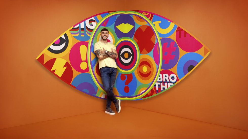 Big Brother 2023 housemate Paul standing in front of the new eye logo with a bright orange background.