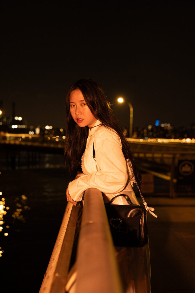 Promotional image for "VIDEO CALL: PM" which sees ÊMIA posing with the New York skyline behind her, leaning against a railing, looking right at the camera.