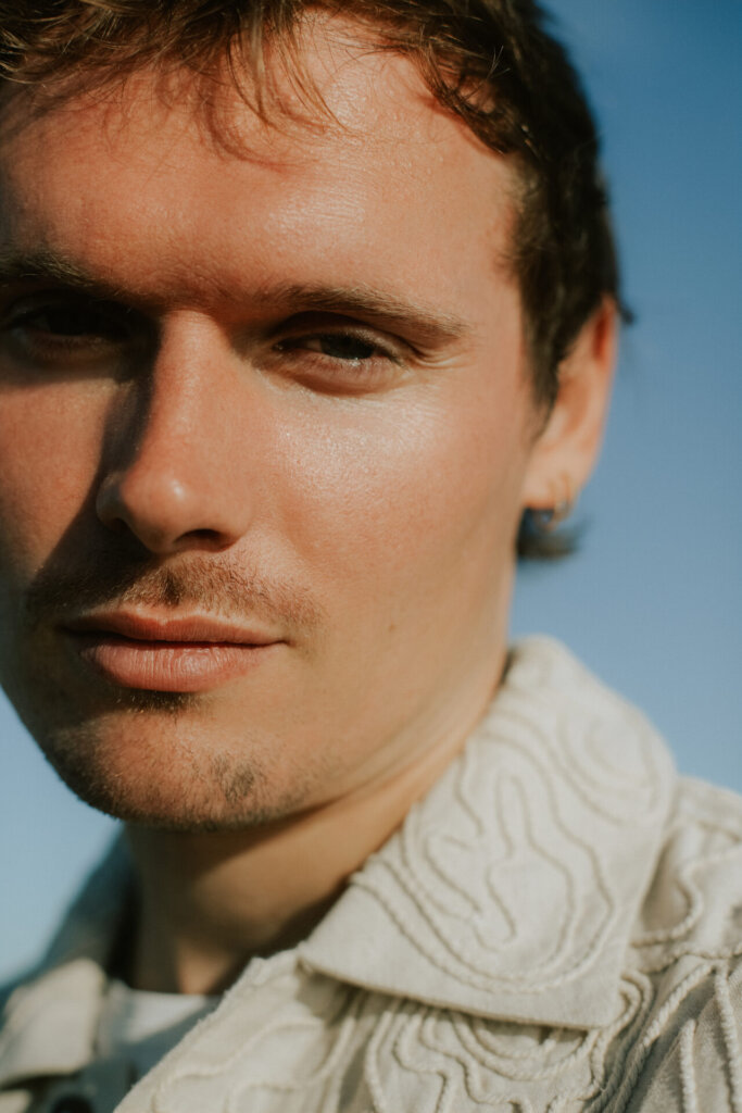 Promotional image for "Nature's Mind" which sees Harry Lloyd from Waiting For Smith, looking directly at the camera in a close-up shot where we see the majority of his face and the collar of his off-white jumper.