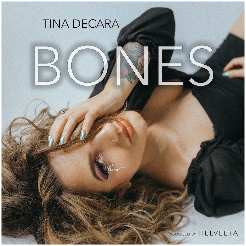 Single cover artwork for "Bones" which sees Tina DeCara lying on the floor with her left hand to her face as silver tears fall from her eyes.