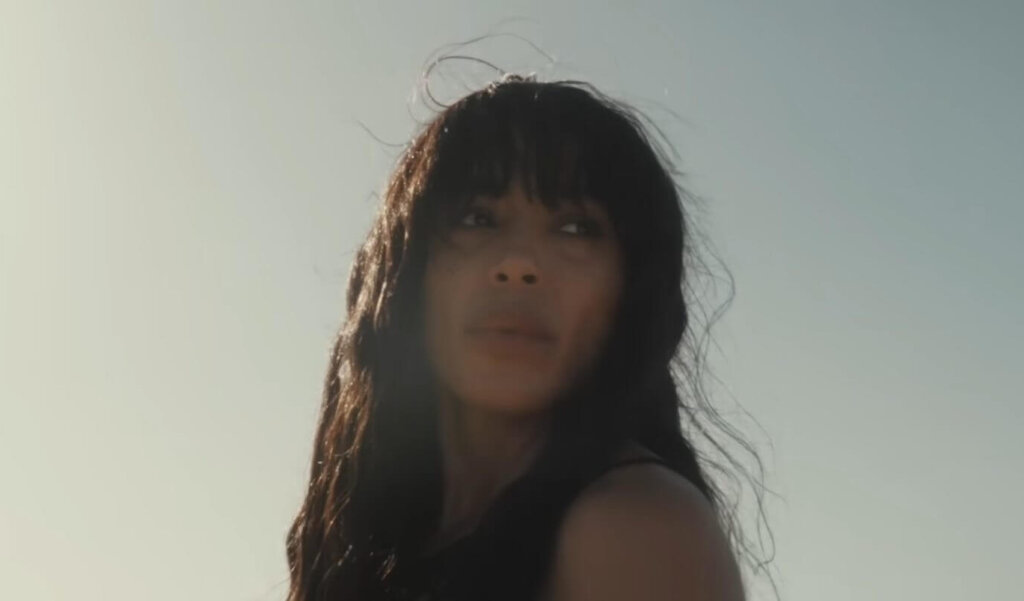 Still from the "Is It Love" music video which sees Loreen looking off to the distance with the sunny sky behind her.