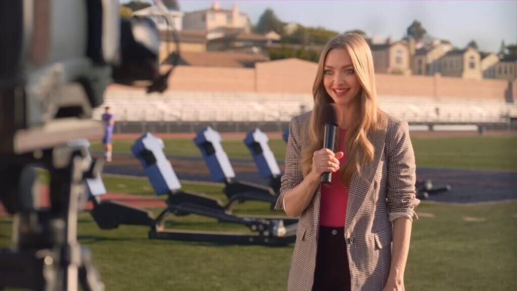 Still from Walmart's Mean Girls reunion advert which sees Amanda Seyfried holding a microphone and presenting the weather.