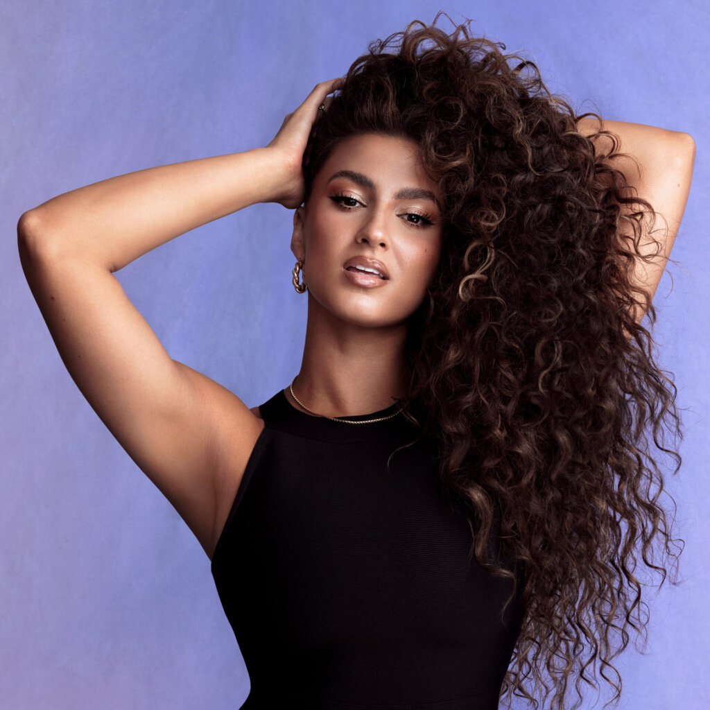 Official album cover artwork for "TORI." which sees Tori Kelly wearing a black top with her hands in her luscious brown curly hair, which is all pulled to the right side over her shoulder.