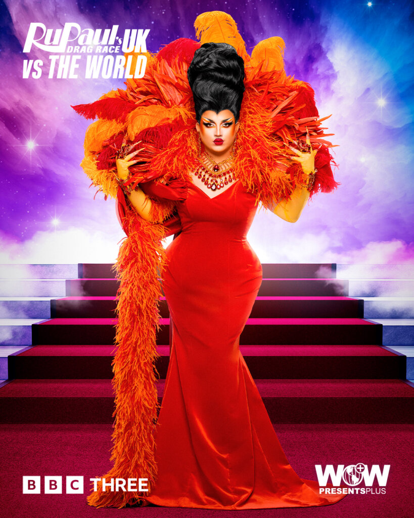 Choriza May from RuPaul's Drag Race UK vs the World series 2, posing in an orange dress and feathered neck piece with a red carpet of stairs behind her.