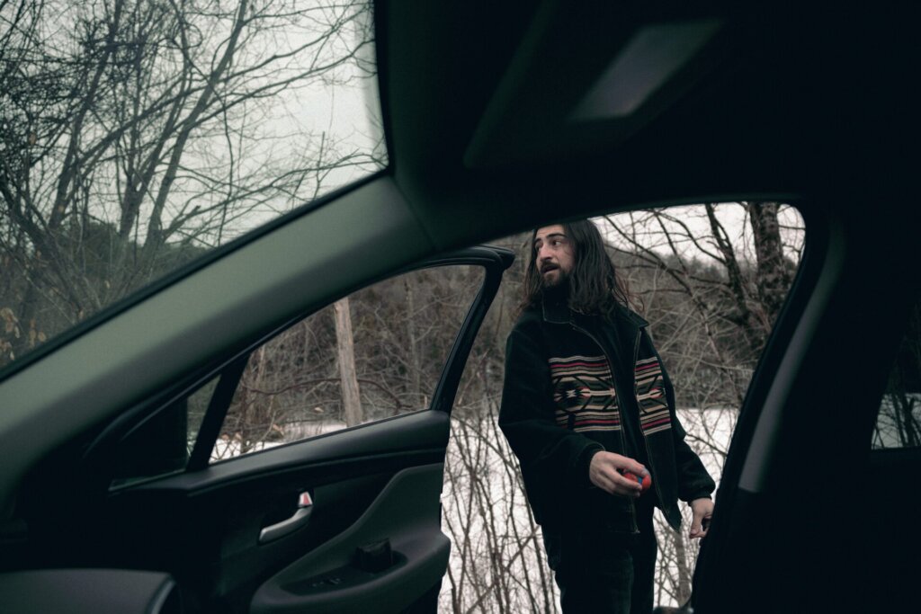 Promotional photo for "Stick Season" which sees the current Chart Double artist, Noah Kahan looking over his shoulder as he is outside a car, while the camera is inside the car.