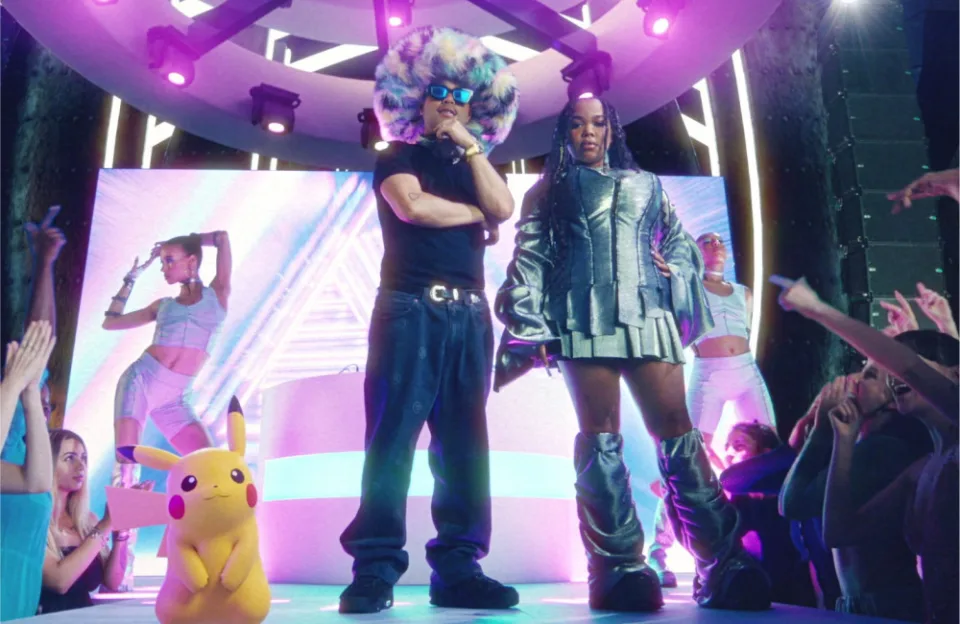 Still from the "Never Be Lonely" music video which sees Jax Jones and Zoe Wees standing on a stage at a stadium with Pikachu standing next to them.