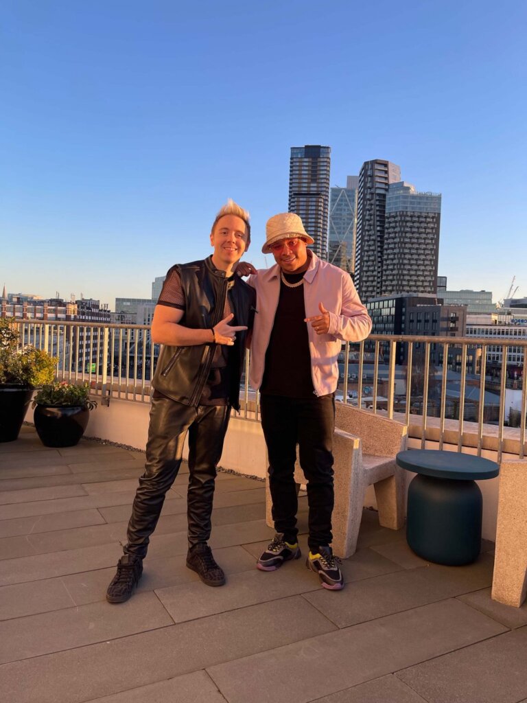 John Galea and Ironik posing together on a balcony overlooking a city.