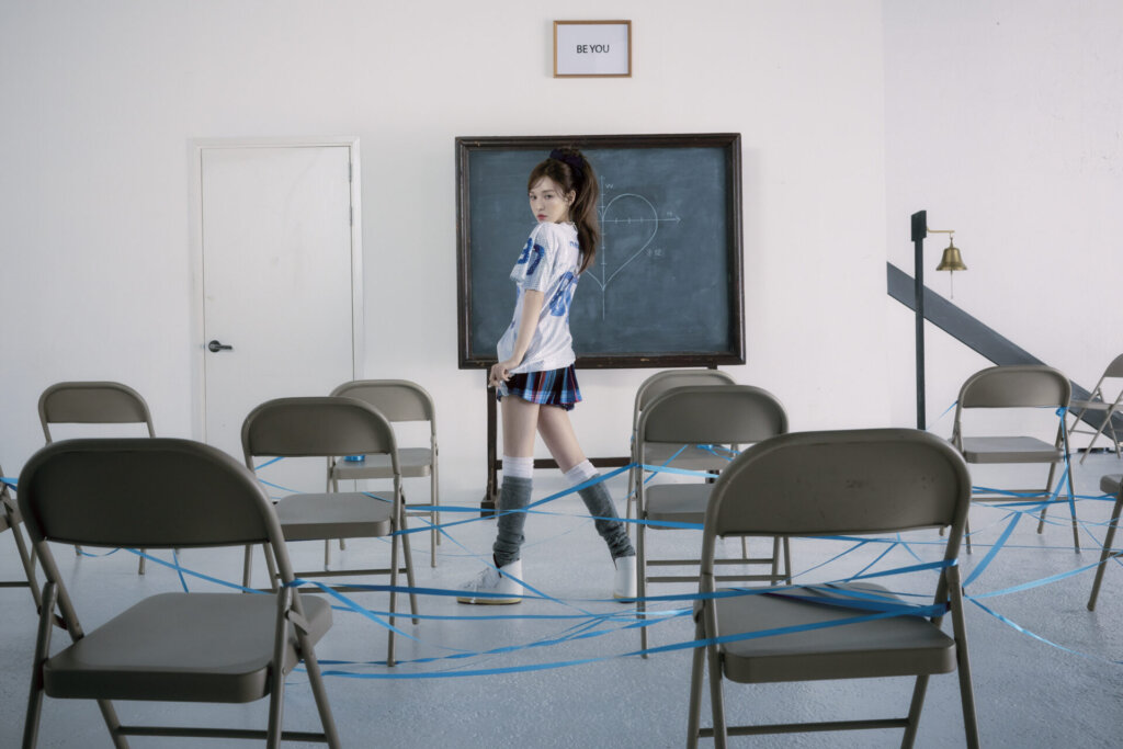 Promotional photo for "Wish You Hell" which sees WENDY in an empty school classroom, standing at the front near the chalkboard, looking over her shoulder at the camera.