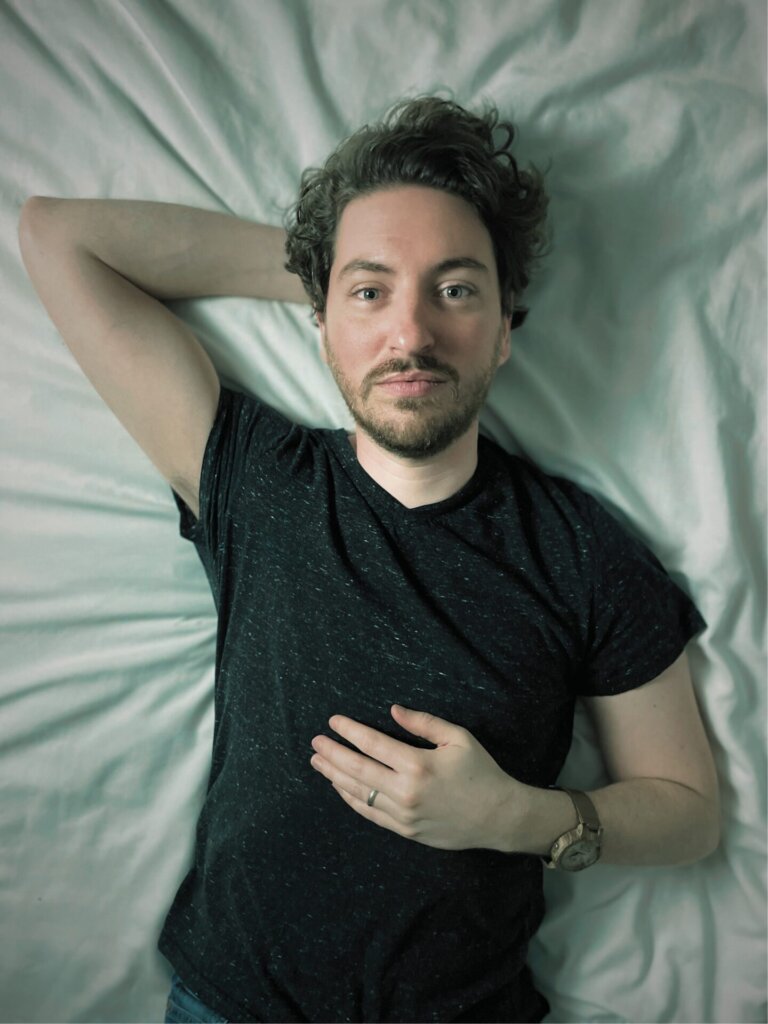 Promotional image for "When The Lights Go Down" which sees the creator of the Sleepwalker project, Kevin Harrison, lying on a bed with an arm behind his head, wearing a black t-shirt.