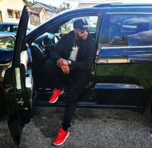 Image of Stephen Thomas stepping out of a black car, wearing a black tracksuit with bright red trainers.