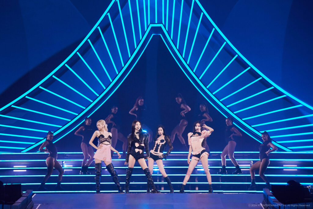 Still from "BLACKPINK WORLD TOUR [BORN PINK] IN CINEMAS" film that sees the four-piece girl group BLACKPINK performing on stage as the lights behind them light up in a blue colour.