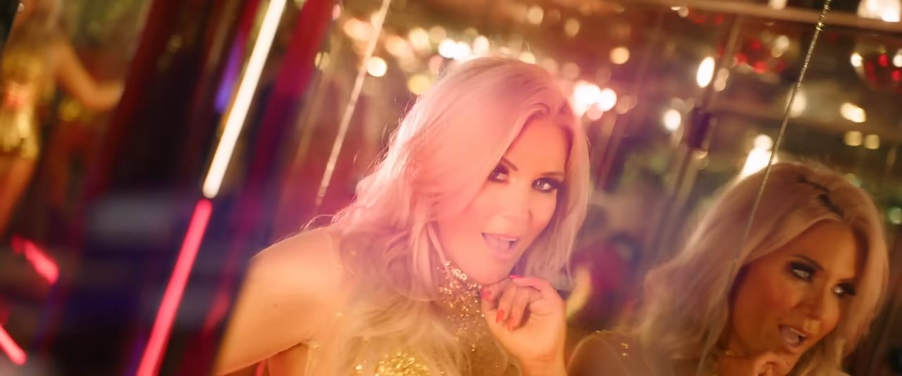 Still from Cascada's "Call Me" music video which sees Natalie Horler performing the song in a gold corset within a mirrored room
