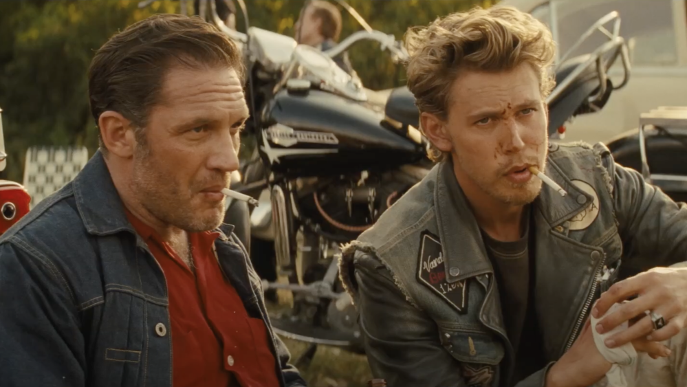 Tom Hardy and Austin Butler as Johnny and Billy, sitting on some grass in front of their motorcycles.