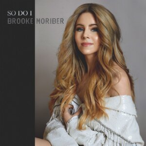 Official single cover artwork for "So Do I" which sees Brooke Moriber looking at the camera, tilted slightly to the left with a cream fringe jacket around her arms.