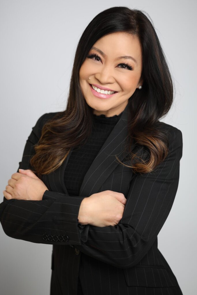 Jen Su posing for a photograph, smiling at the camera with her arms folded while wearing a black jacket.