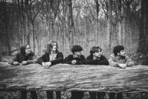 Black and white photo of SAMSARA. the band, all posing in the woods behind a log that is on its side.