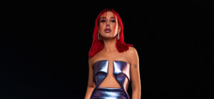 Promotional photo of SHADU with her red hair at shoulder length, wearing a metallic dress.