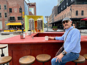 Denim Dan's frontman Michael Halitzer sitting on a stool at an outdoor cafe.