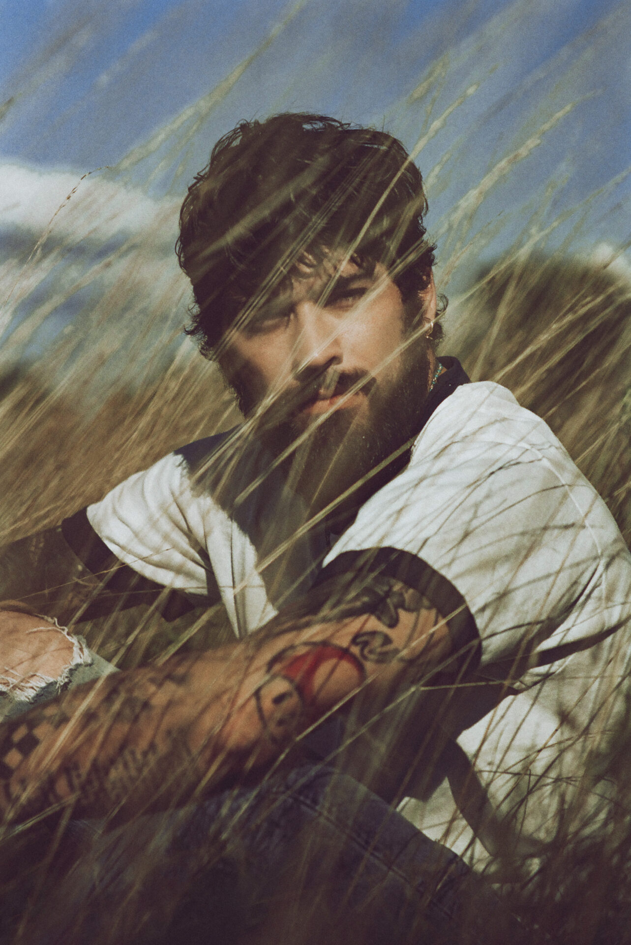 Promotional photo for Stairway to the Sky Tour which shows a mid-shot of ZAYN sitting in the grass wearing a white t-shirt.