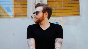 A mid-shot of Michael Burke facing towards the camera with his head turned completely to the left. He's wearing sunglasses and a black t-shirt.