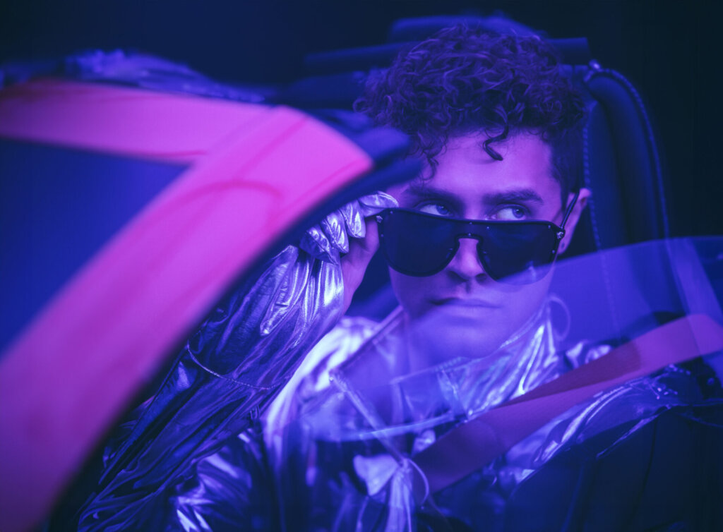 Stewart Taylor in the front seat of a pink Corvette, pulling his shades down slightly as he looks out the window.