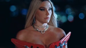 Still from the "Joyride" music video which sees a headshot of Kesha after she's stepped out of the car, wearing a red leather outfit and a gorgeous necklace.