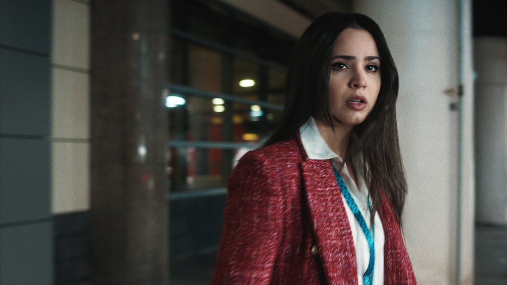 Still from Netflix's Carry-On trailer which sees Sofia Carson in a red jacket and a white shirt, outside looking scared.