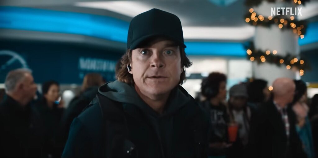 Still from Netflix's Carry-On trailer which sees Jason Bateman as the Mysterious Traveller, dressed in black clothes and wearing a black baseball cap.