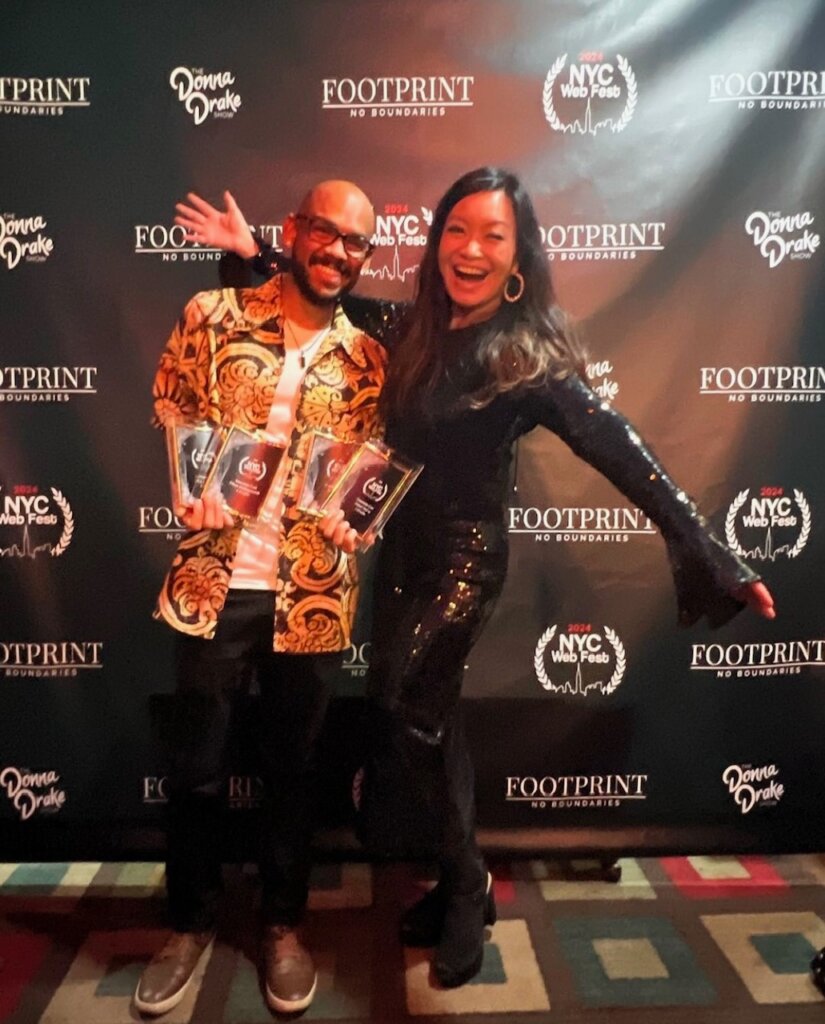 Jen Su & Todd A. Jackson posing in front of the NYC Web Fest logo banner which also has Donna Drake and Footprint Network logos on.