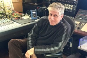 Phil Lentz sitting on a chair in the studio, wearing a black jumper.