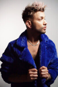 Jaime Adrian posing shirtless with a large blue fluffy coat on similar to the one Jade Thirlwall wears in her "Angel of my Dreams" music video.