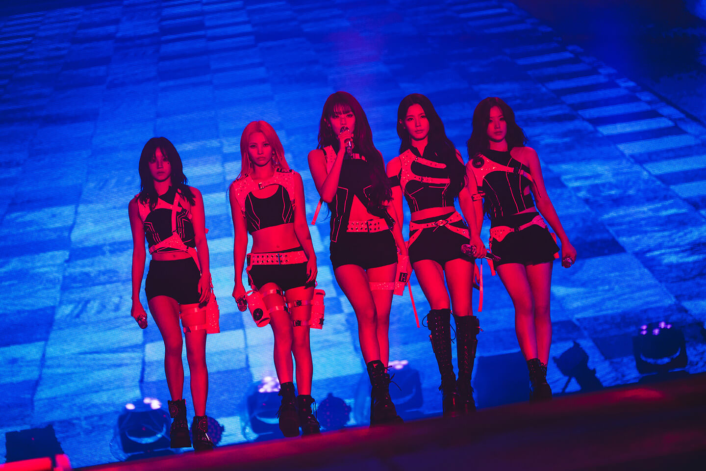 Still from (G)I-DLE WORLD TOUR [iDOL] IN CINEMAS where girl group (G)I-DLE is performing on stage in black outfits.